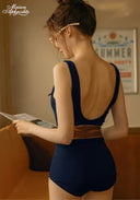 Navy one-piece swimsuit with open back and thin shoulder straps, brown waist belt