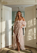 A woman models a pale blush pink ruffled off-the-shoulder maxi dress in a sunlit room with open white doors and a chandelier in the background. The brand name 'Aurelien Affected' is visible in the top left corner.