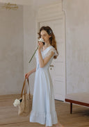 White V-neck lace midi dress with ruffled shoulders and flared skirt, holding a bag