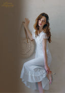 White lace midi dress with ruffled cap sleeves and flared skirt, holding a bag
