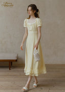 Romance dress in pale yellow with short puff sleeves and ruffled skirt, holding white woven bag