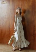 Floral tiered maxi sundress with thin straps and tiered ruffle skirt, holding woven bag