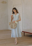 White lace midi dress with cap sleeves and ruffled hem, holding a woven straw bag
