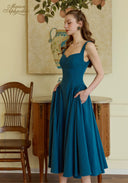 Teal blue suspender dress with spaghetti straps and pleated skirt in a side view.