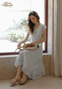 White lace midi dress with short sleeves and ruffle trim, seated and holding a bag