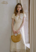 Lace tea dress in pale yellow with lace-trimmed V-neck and puff sleeves, holding straw bag