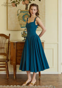 Teal blue suspender dress with square neckline and pleated midi skirt, standing pose.