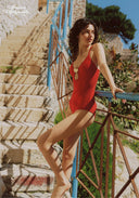 Red one-piece swimsuit with thin straps and decorative gold charm at the bust
