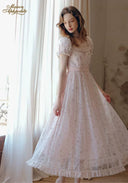 Light pink floral tea dress with square neckline lace trim and puff sleeves; standing three-quarter view.
