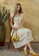Cream lace embroidered dress with square neckline, cap sleeves, and flowing tiered skirt.