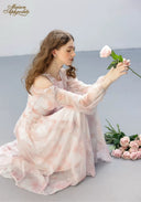 Floral tiered dress in pale pink with ruffled sleeves, crouching side view with bouquet