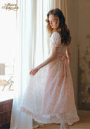 Light pink floral tea dress with lace cap sleeves and ribbon waist tie; side view while standing.