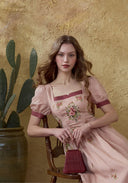 Pink linen maxi dress with burgundy cap sleeves and floral embroidery, seated pose