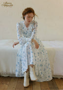 Blue floral tiered maxi dress with long sleeves and layered skirt, seated pose.