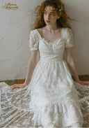 White lace dress with square neckline, puff sleeves, and layered skirt with scalloped hem.