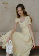 Romance dress in pale yellow with lace-trim neckline, puff sleeves, and gathered skirt, seated