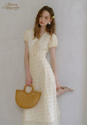 Lace tea dress in pale yellow with V-neck and short puff sleeves, side view with straw bag