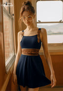 Navy swimdress with square neckline, shoulder ties, tan braided belt, and flared skirt
