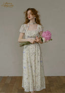 Woman in a floral dress holding flowers against a plain background
