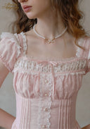 Pale pink dotted dress bodice with lace trim, front buttons, and pearl necklace