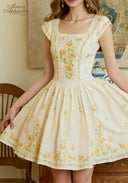 Cream linen dress close-up: yellow floral embroidery, square neckline, pleated gathered skirt.