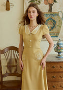 Yellow embroidered dress close-up with peter pan collar, button placket, and chest motifs