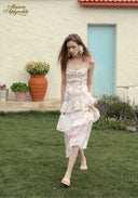 Woman in a floral dress standing on grass with a building and plants in the background