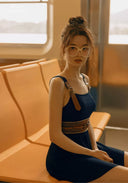 Navy swimdress with square neckline, layered straps, and tan braided waist belt