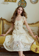 Cream lace embroidered dress with square neckline, shoulder ruffles, and full tiered skirt.