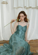 Teal satin midi dress with ruched bodice and spaghetti straps, seated pose