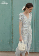 Blue Celeste floral dress with V-neck and tassel fringe sleeves, holding woven bag
