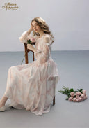 Floral tiered dress in pale pink with long ruffles and sheer layers, seated pose