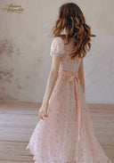 Light pink floral tea dress, back view with ribbon waist tie and tiered lace hem; walking pose.