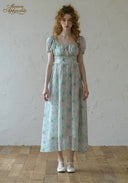 Woman wearing a floral dress standing against a plain wall.