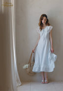 White lace midi dress with cap sleeves and ruffled hem, holding a woven straw bag