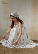 Secret Garden dress in white with floral print, tiered skirt; wearing matching bonnet