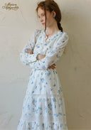 Blue floral tiered maxi dress with long sleeves and square neckline, crossed-arm pose.