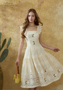 Cream lace embroidered dress with square neckline, cap sleeves, and gathered tiered skirt.