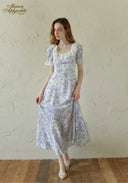 Woman wearing a floral dress standing against a textured white wall.