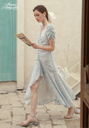 Blue Celeste floral dress with V-neck and flowing midi skirt, carrying woven handbag