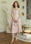 Woman in a pink dress holding a matching handbag in an elegant room.